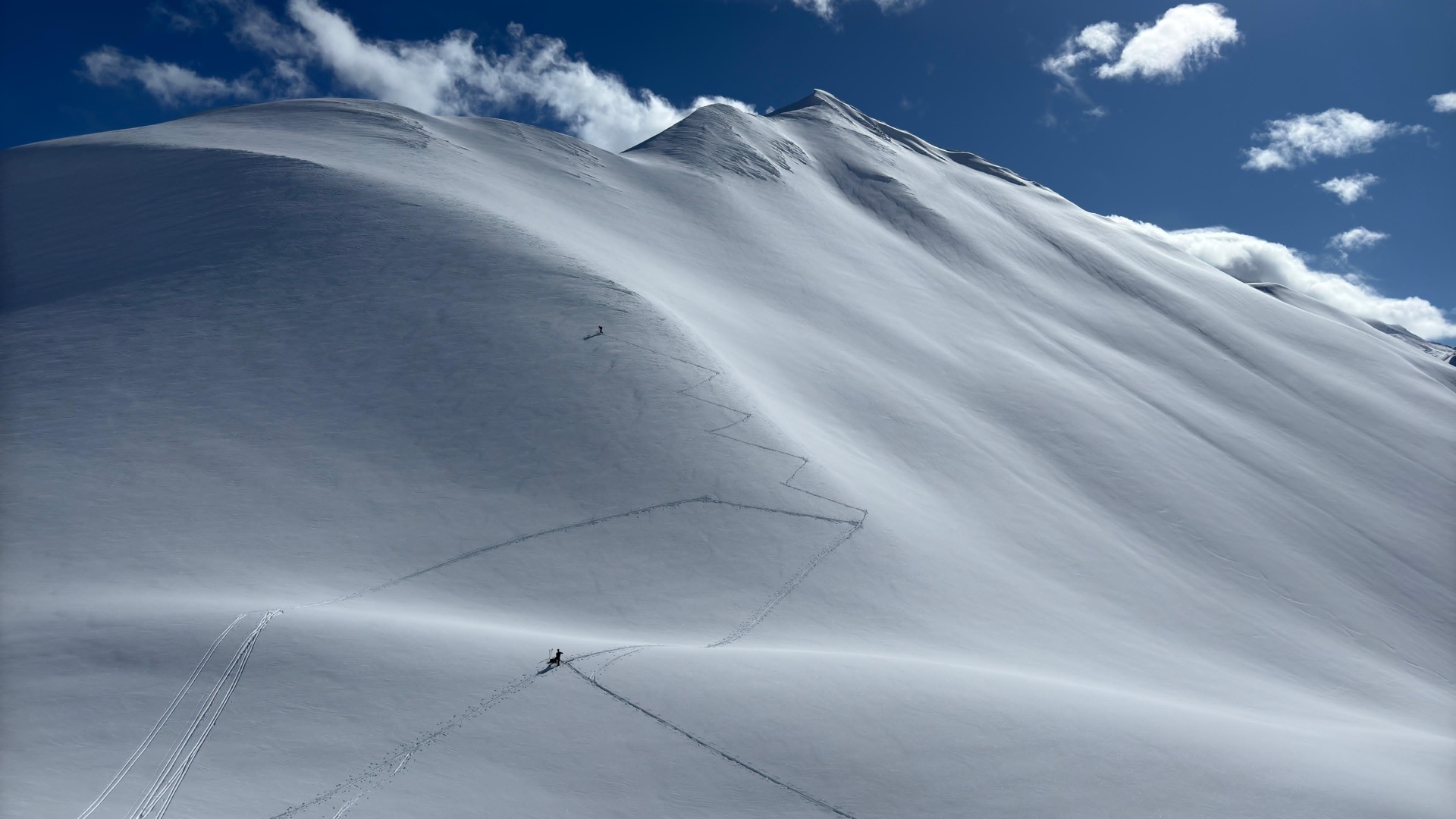 Skifahrer steigt einen verschneiten Berg hinauf unter strahlend blauem Himmel.