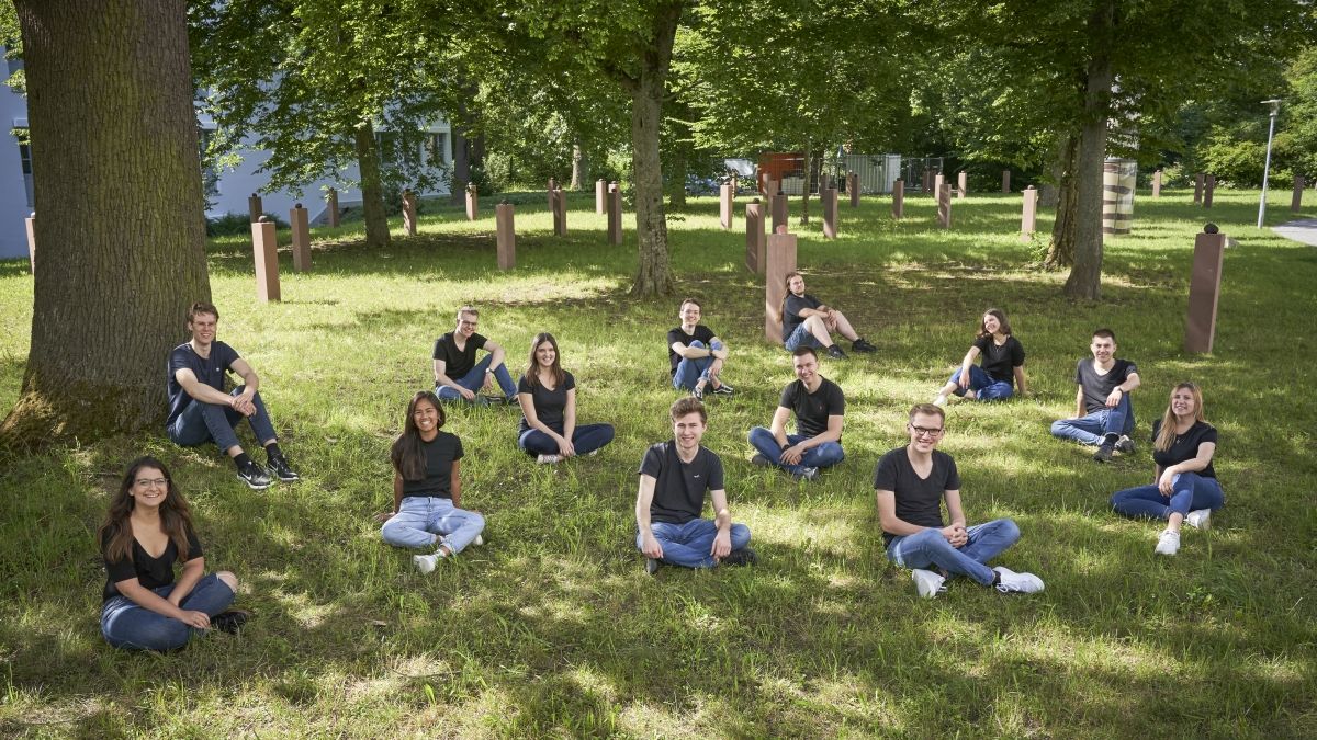 Mitglieder posieren sitzend auf einer Wiese für ein Gruppenbild.