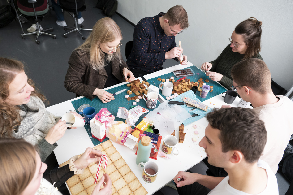 Mehrere Menschen sitzen an einem Tisch und arbeiten an Lebkuchen. 