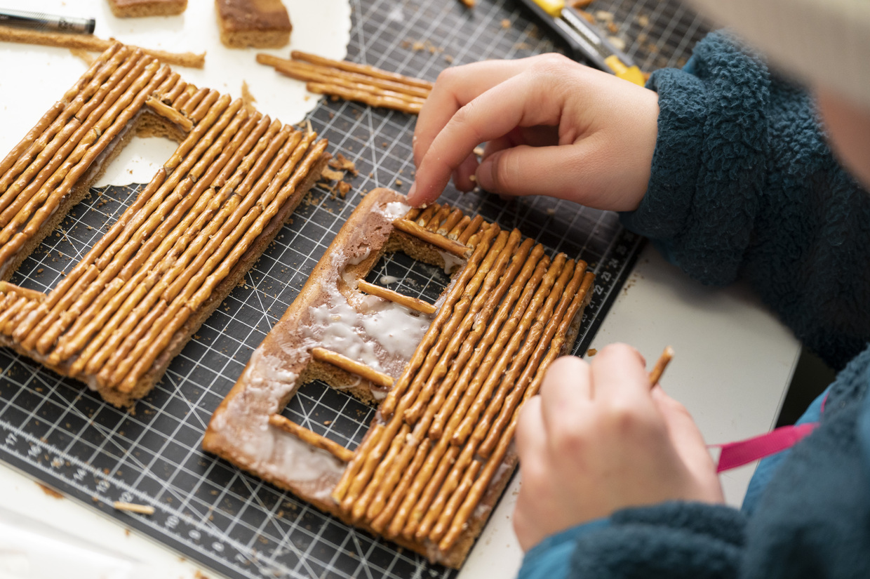 Eine Person beklebt die Seite eines Lebkuchenhauses mit Salzstangen. 