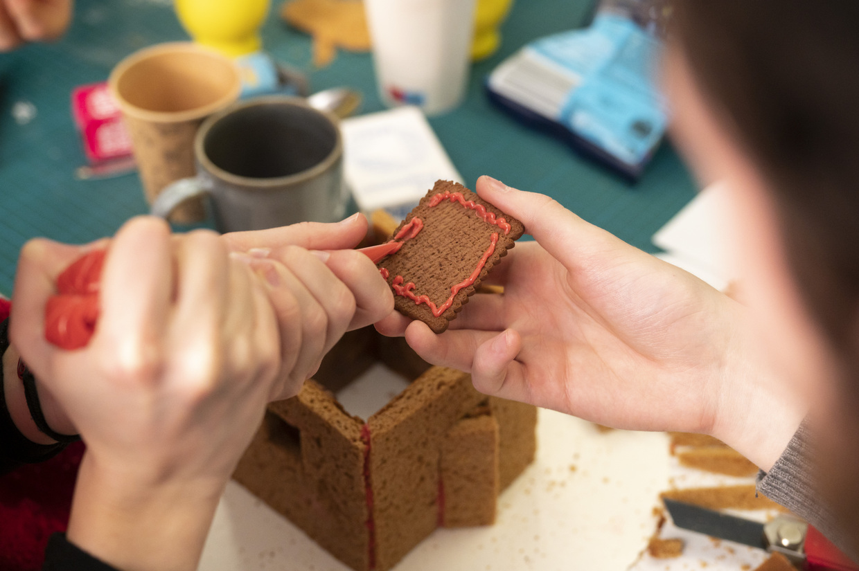 Eine Person hält ein Stück Lebkuchen, wärhrend eine andere Person roten Zucker aufträgt. 