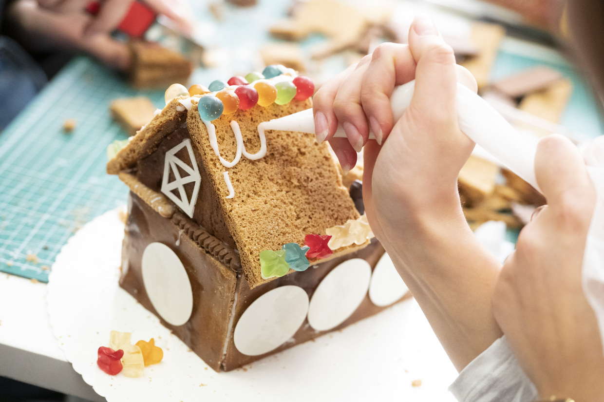Ein fast fertiges Lebkuchenhaus, dem mit weißen Zuckerguss Dachziegel gezaubert werden. 