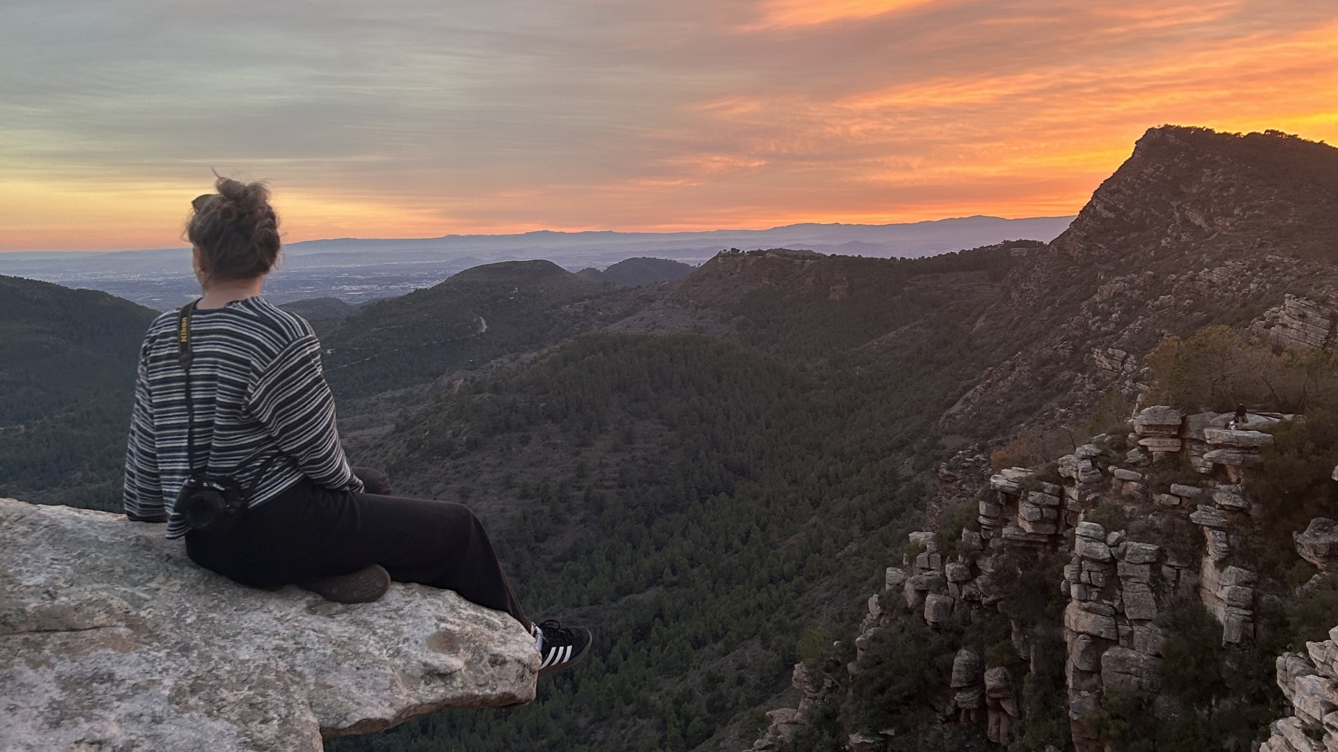 Susan sitzt auf einem Felsvorsprung und schaut in den Sonnenuntergang. 