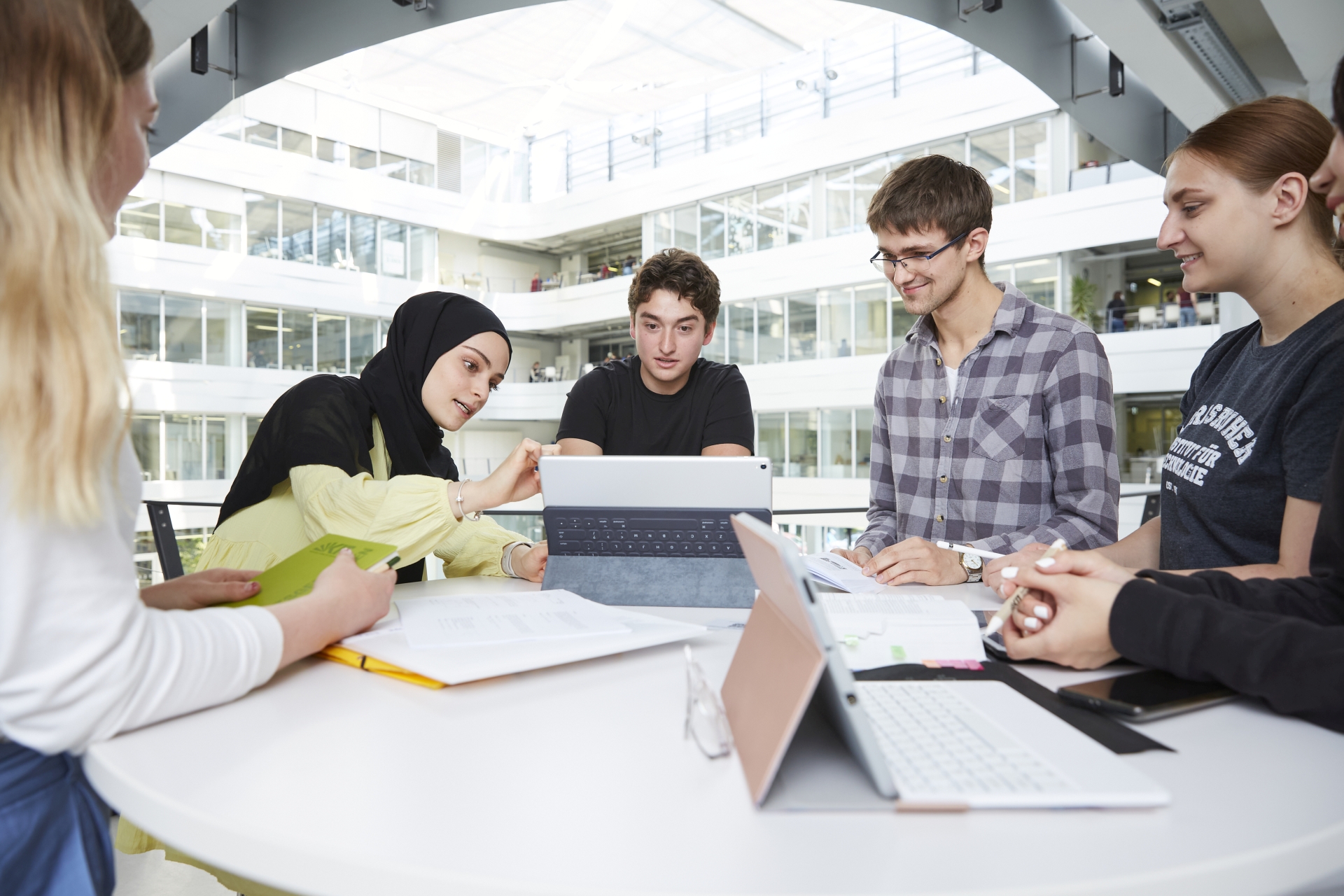 Mehrere Studierende stehen an einem Tisch und lernen. Eine von ihnen erklärt den Anderen etwas. 