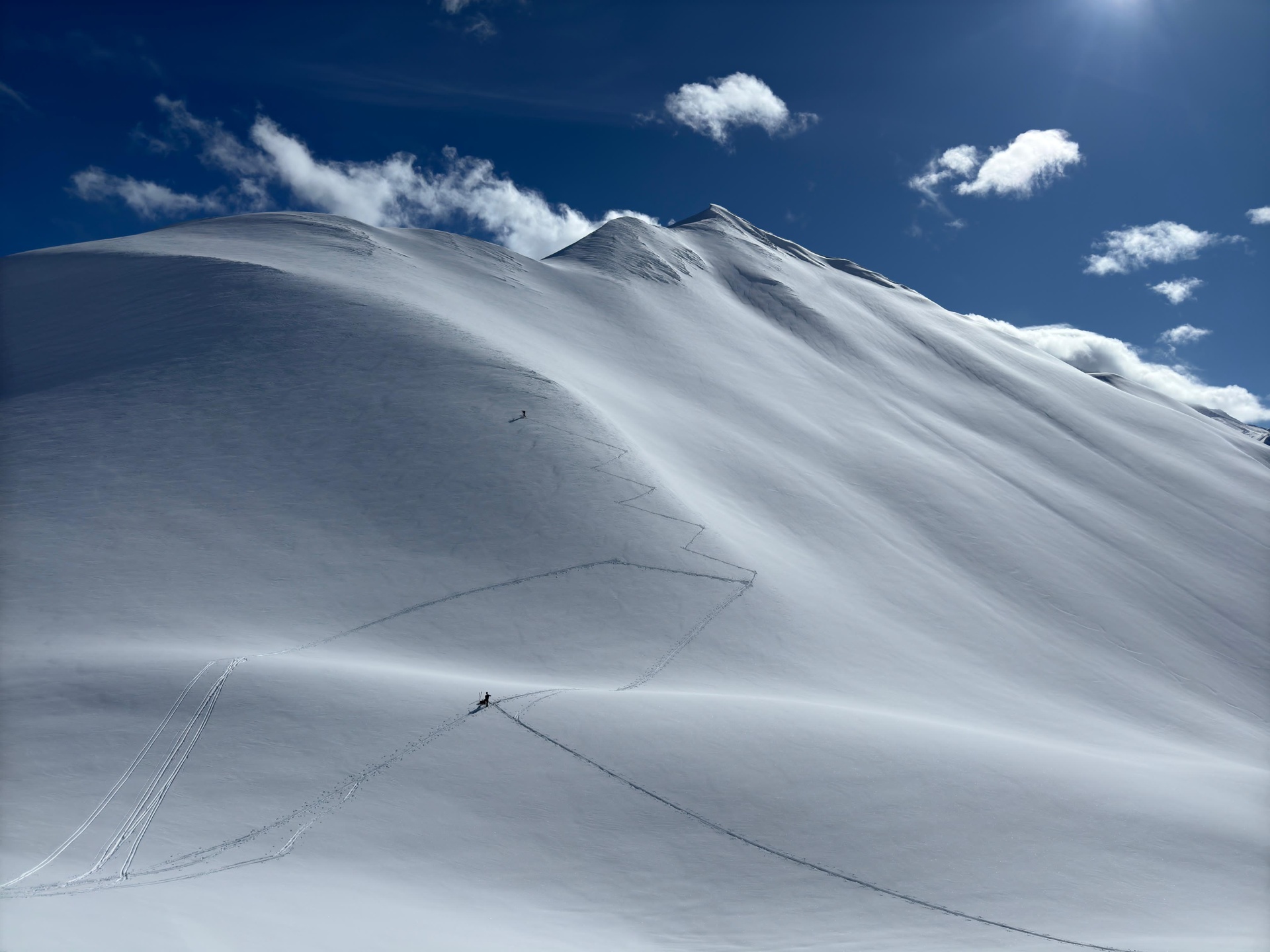 Ein Skifahrer hinterlässt Spuren im unberührten Schnee auf einem sonnigen Berggipfel.