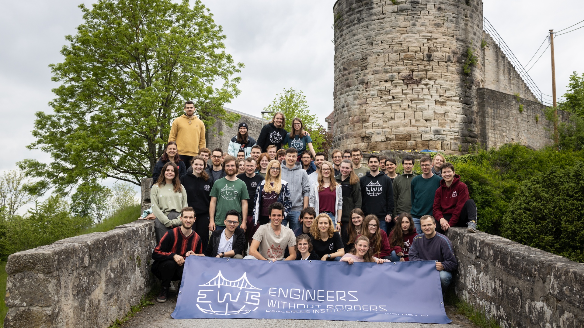 Eine Gruppe von Menschen posiert vor einer alten Burg mit einem „Engineers Without Borders“-Banner.