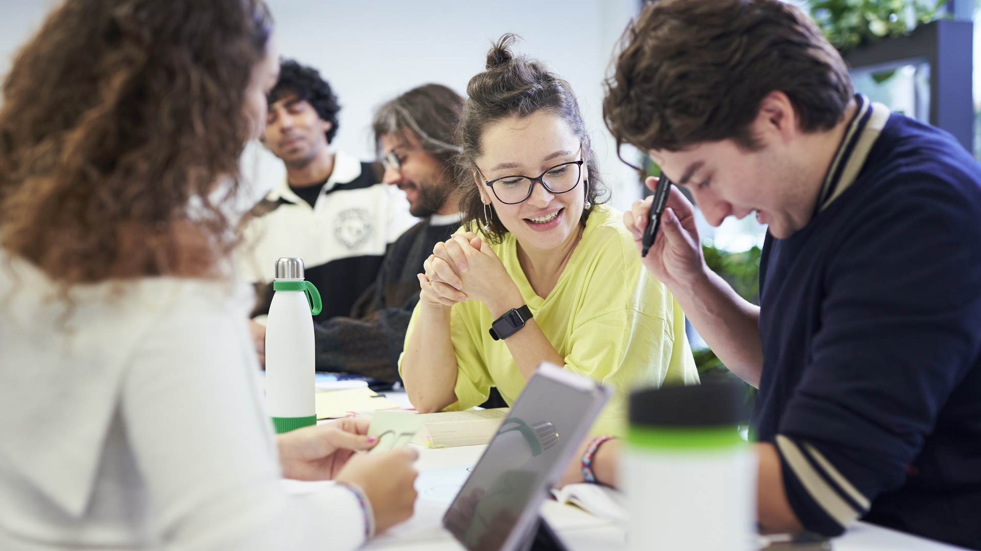 Mehrere Studierende sitzen in Gruppen an Tischen und unterhalten sich.