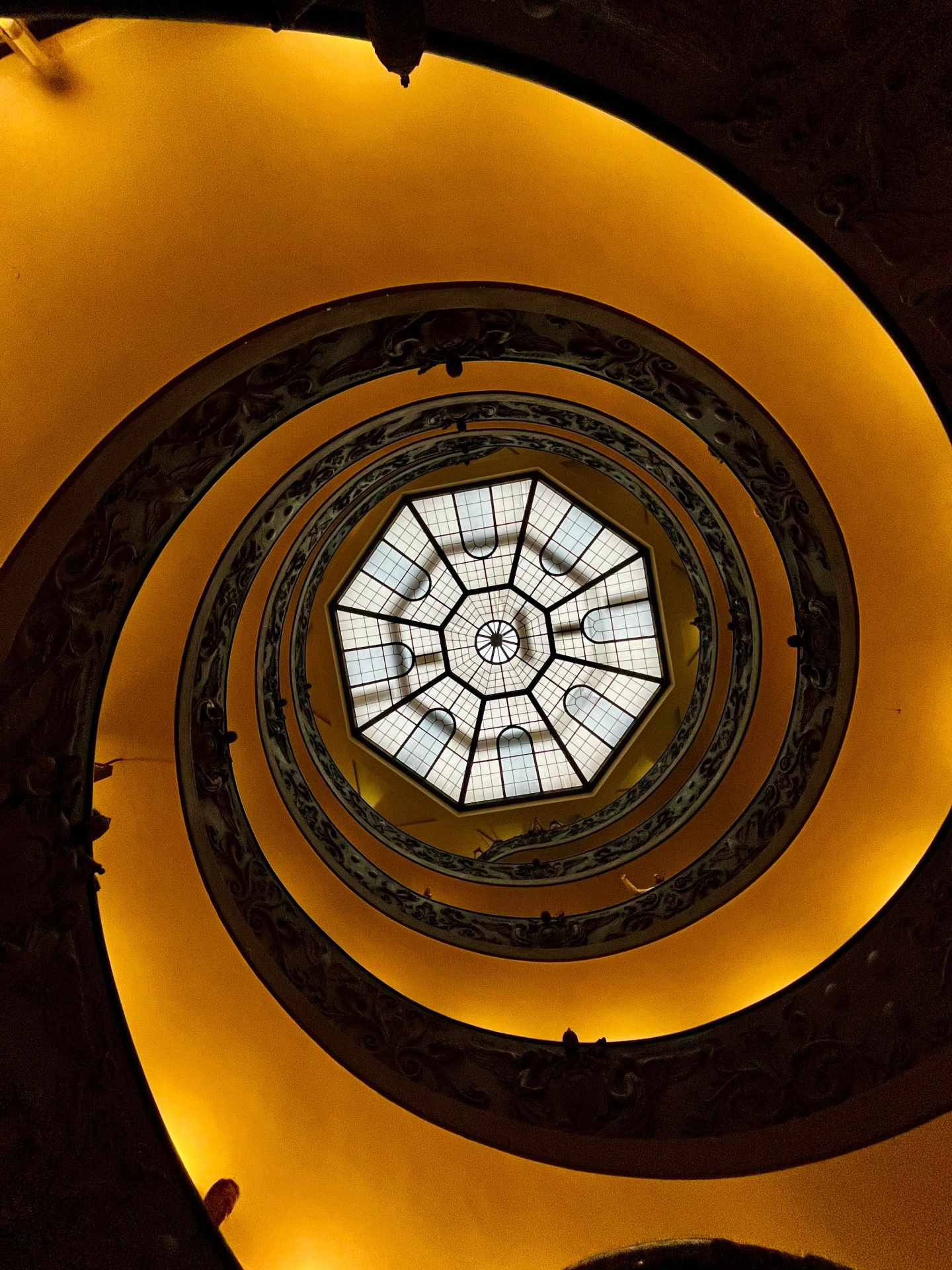 Blick in eine spiralförmige Treppe mit Glasdach von unten.