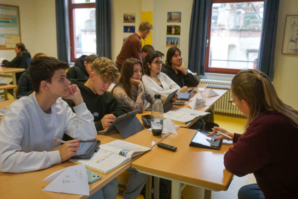 Die Klasse sitzt an ihren Tischen, während der Lehrer durch die Reihen geht.