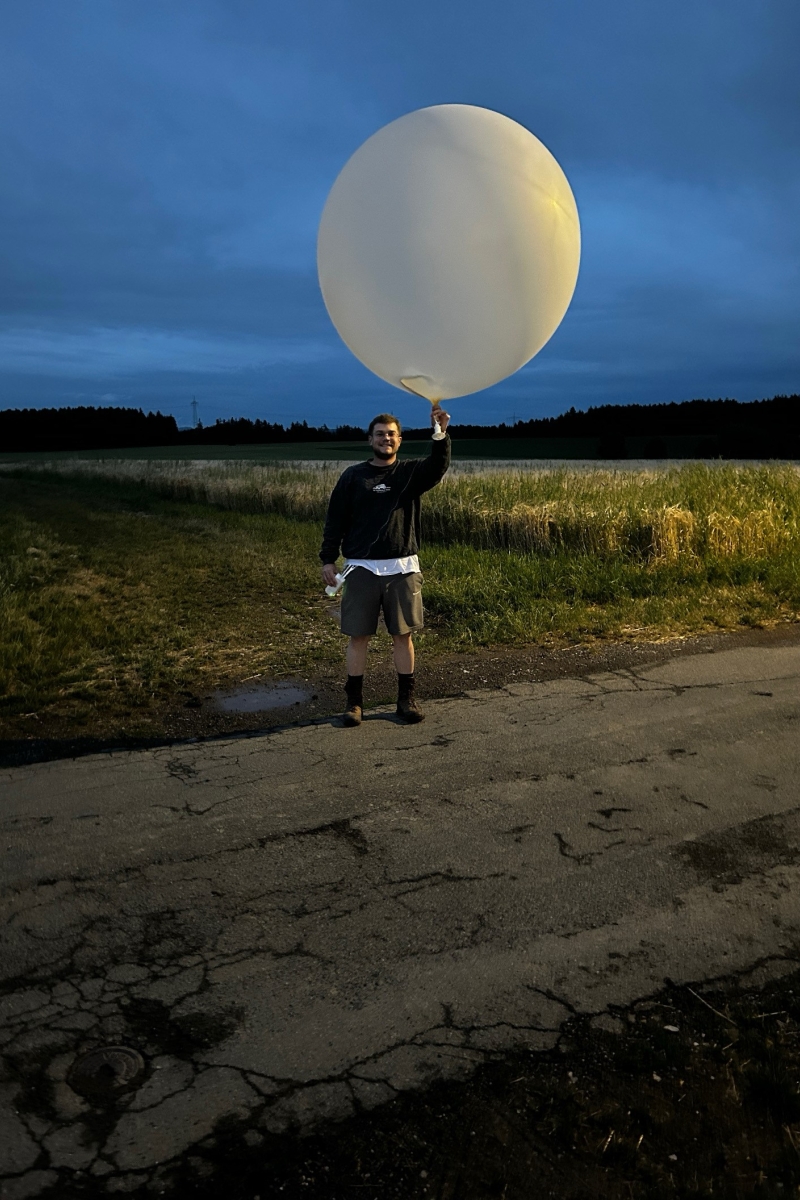 Max Schaub posiert mit einem Wetterballon in der Hand bei der Dämmerung.