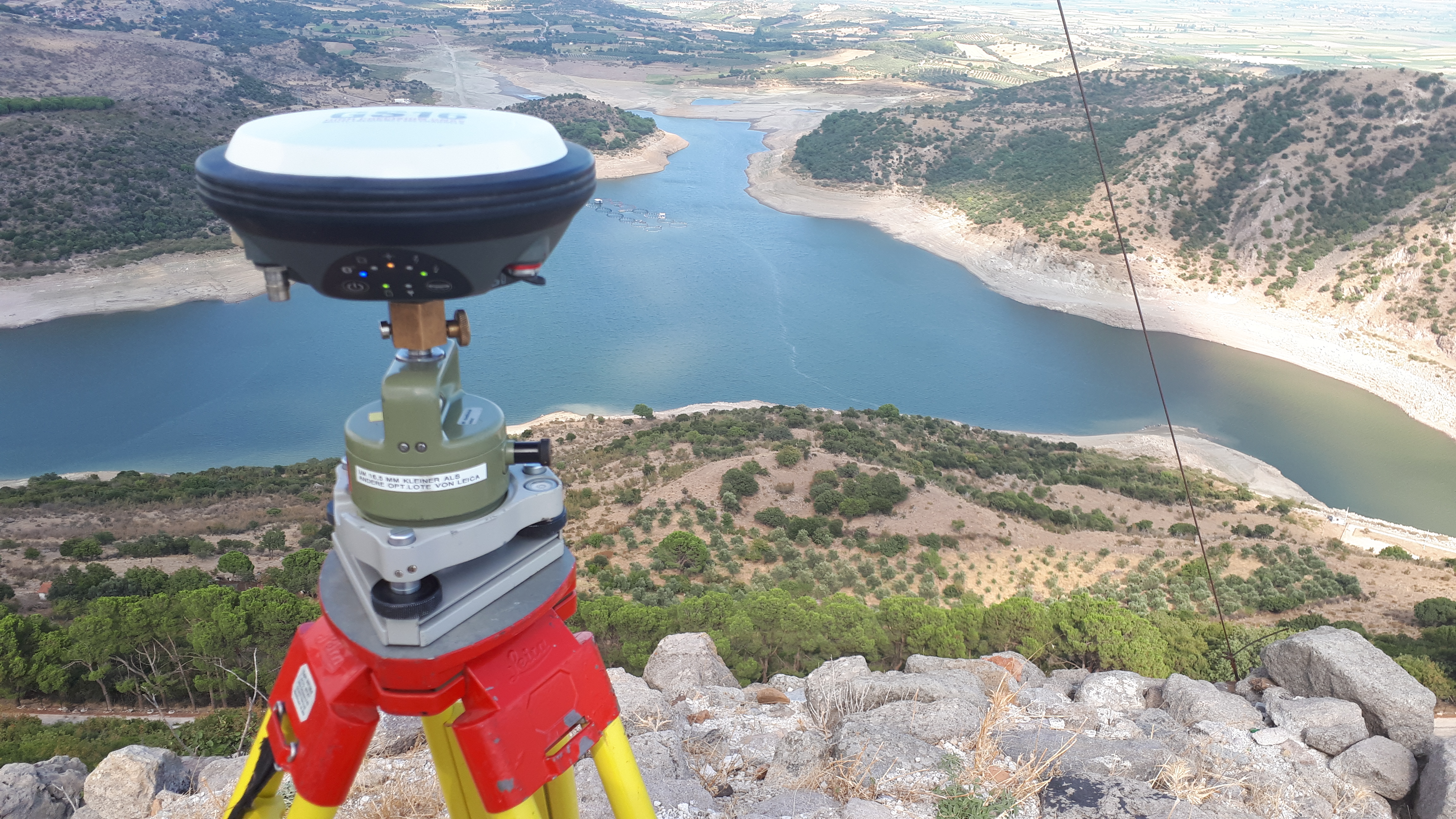 Ein Messinstrument steht an einem Hang. Im Hintergrund ist ein See und Berge. 