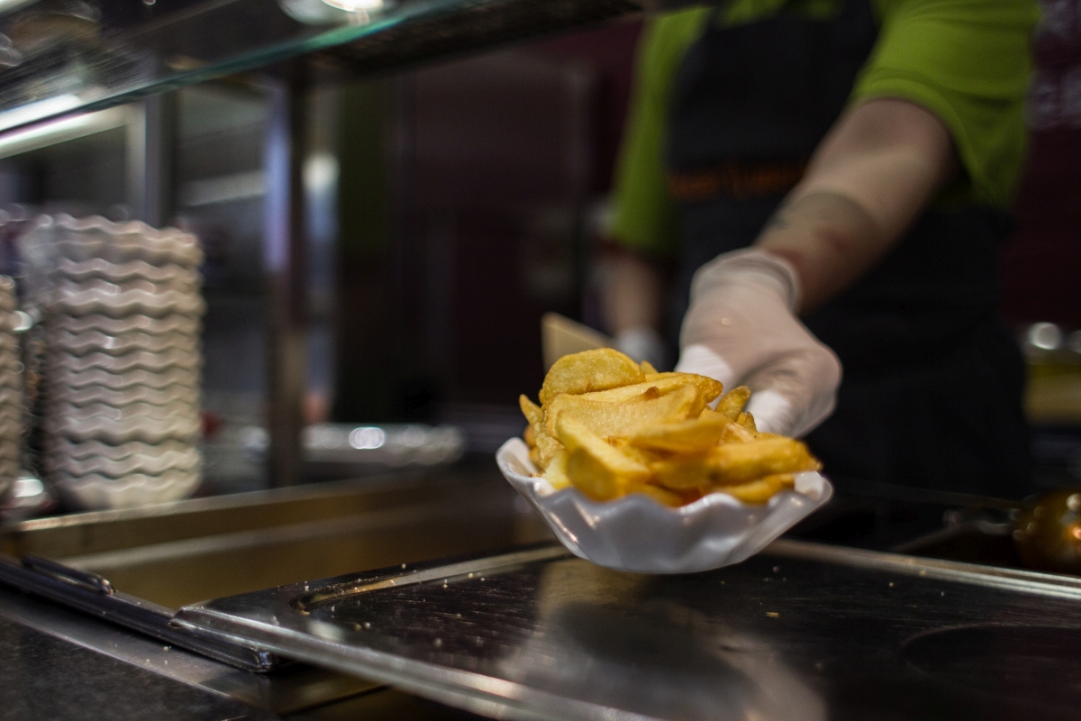 Eine behandschuhte Hand reicht eine Portion Pommes nach vorn. 