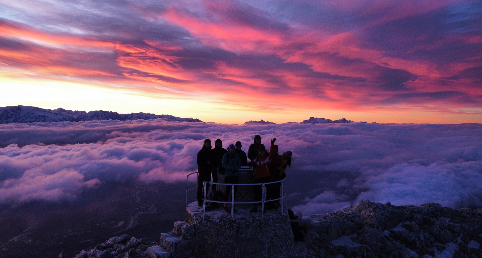 Gruppe von Menschen genießt einen lebhaften Sonnenuntergang über den Wolken.