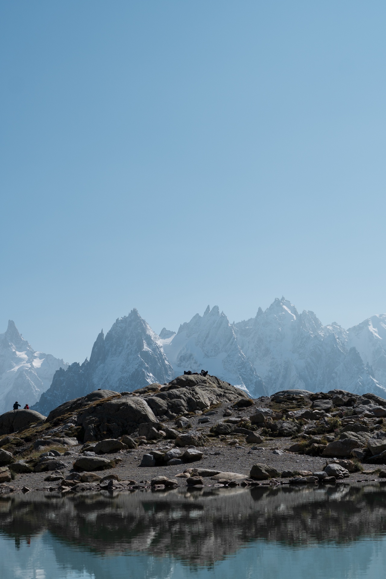 Berglandschaft mit klarer Spiegelung im See und schneebedeckten Gipfeln im Hintergrund.
