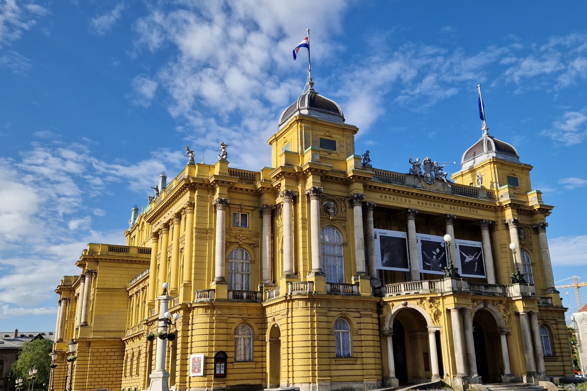 Au&szlig;enansicht des gelben Kroatischen Nationaltheaters in Zagreb unter blauem Himmel.