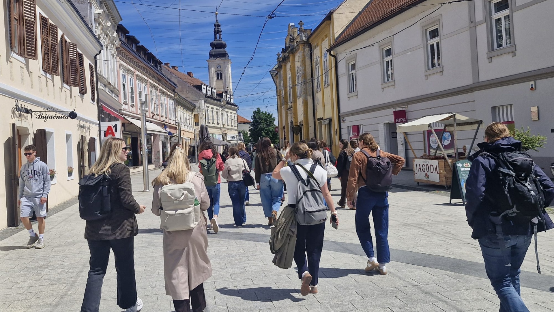 Students with backpacks walking down a pedestrian street in a European town.