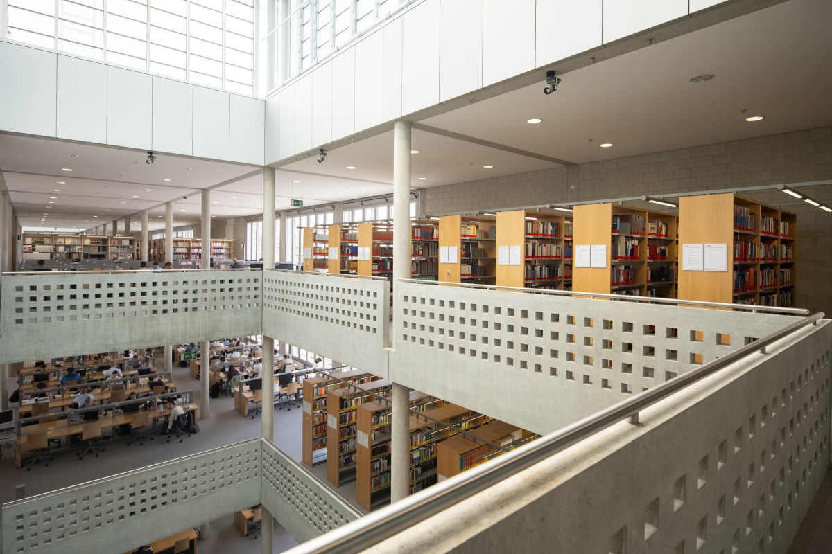 Moderner, heller Bibliotheksraum mit mehreren Etagen, B&uuml;cherregalen und Arbeitspl&auml;tzen.