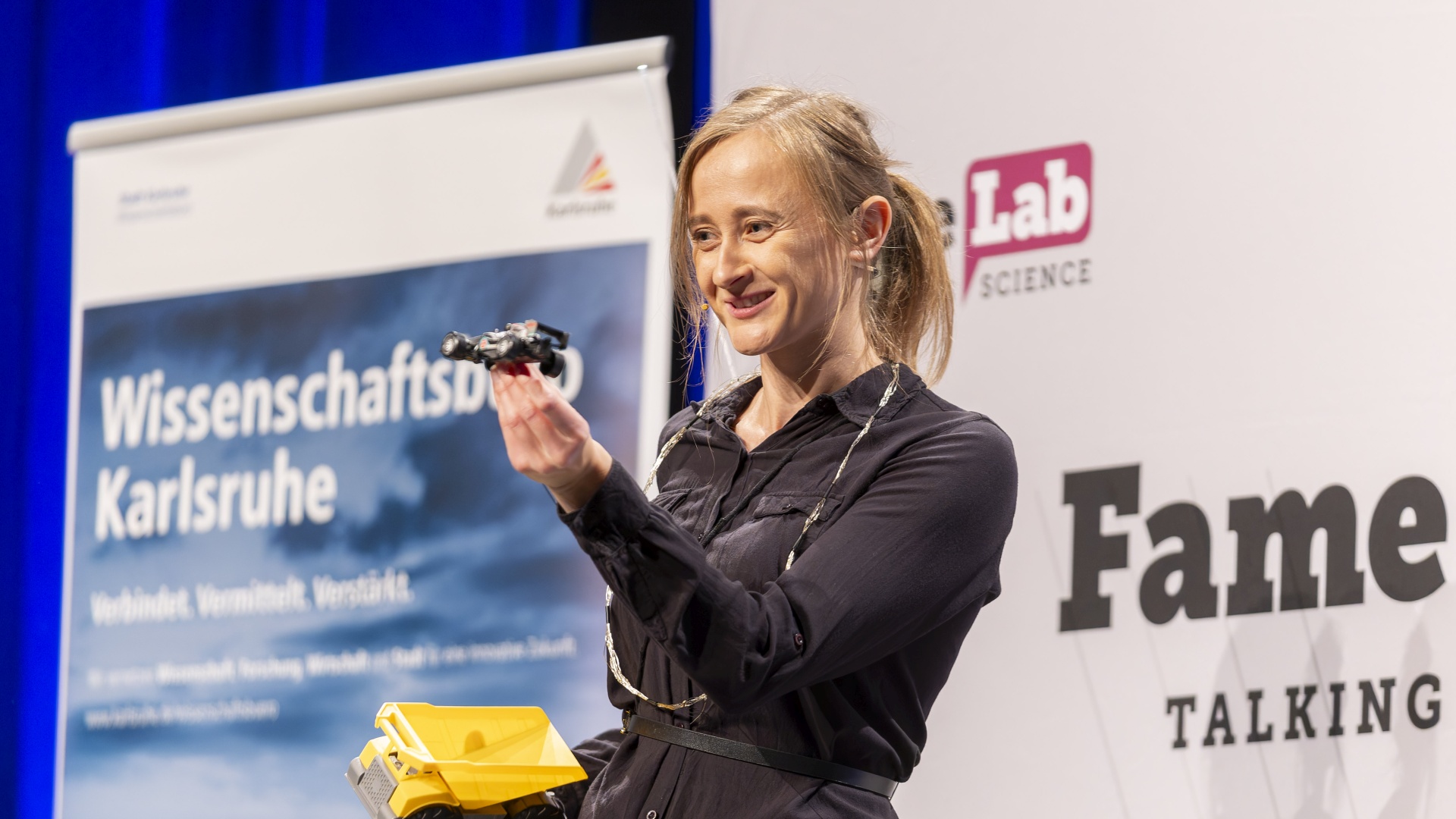 Maria Paszkiewicz-Idzik hält ein Modellfahrzeug während ihres FameLab-Vortrags in die Höhe.