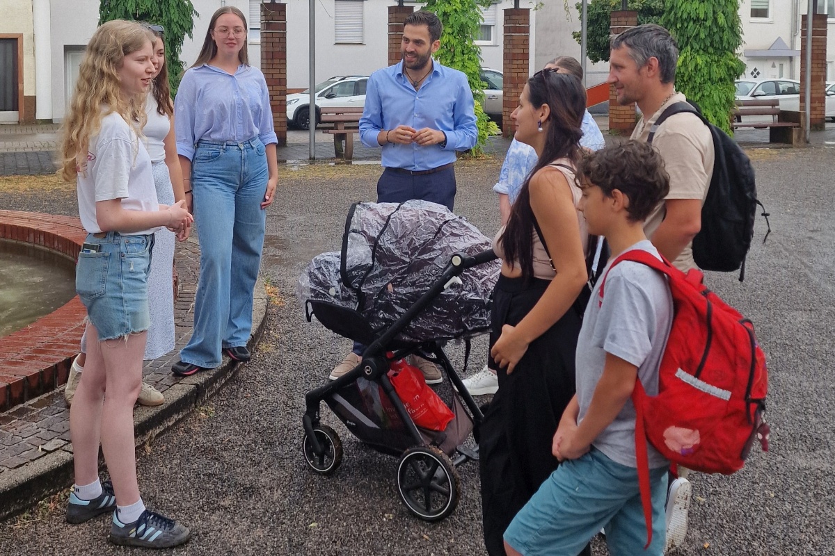 Gruppe von Erwachsenen und Jugendlichen mit Kinderwagen im Gespr&auml;ch im Freien.