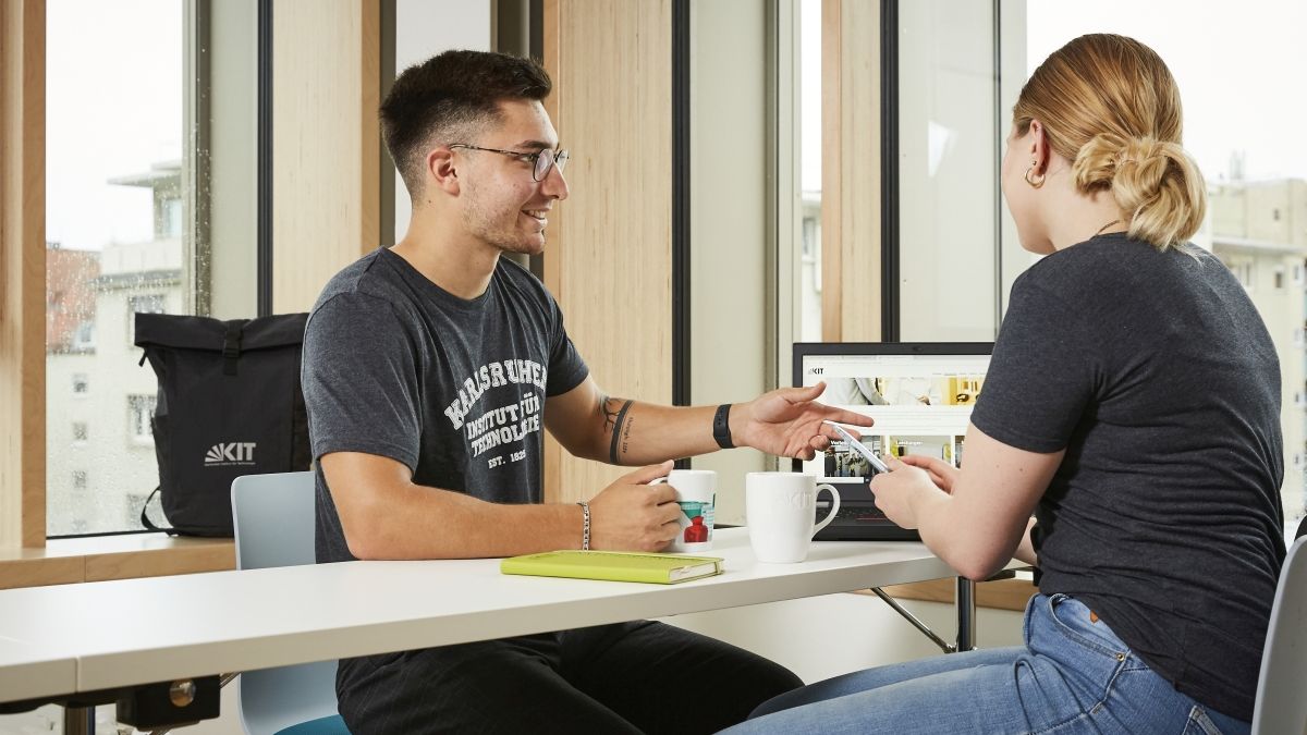 Zwei Studierende sitzen gemeinsam an einem Tisch vor einem Laptop und lernen.