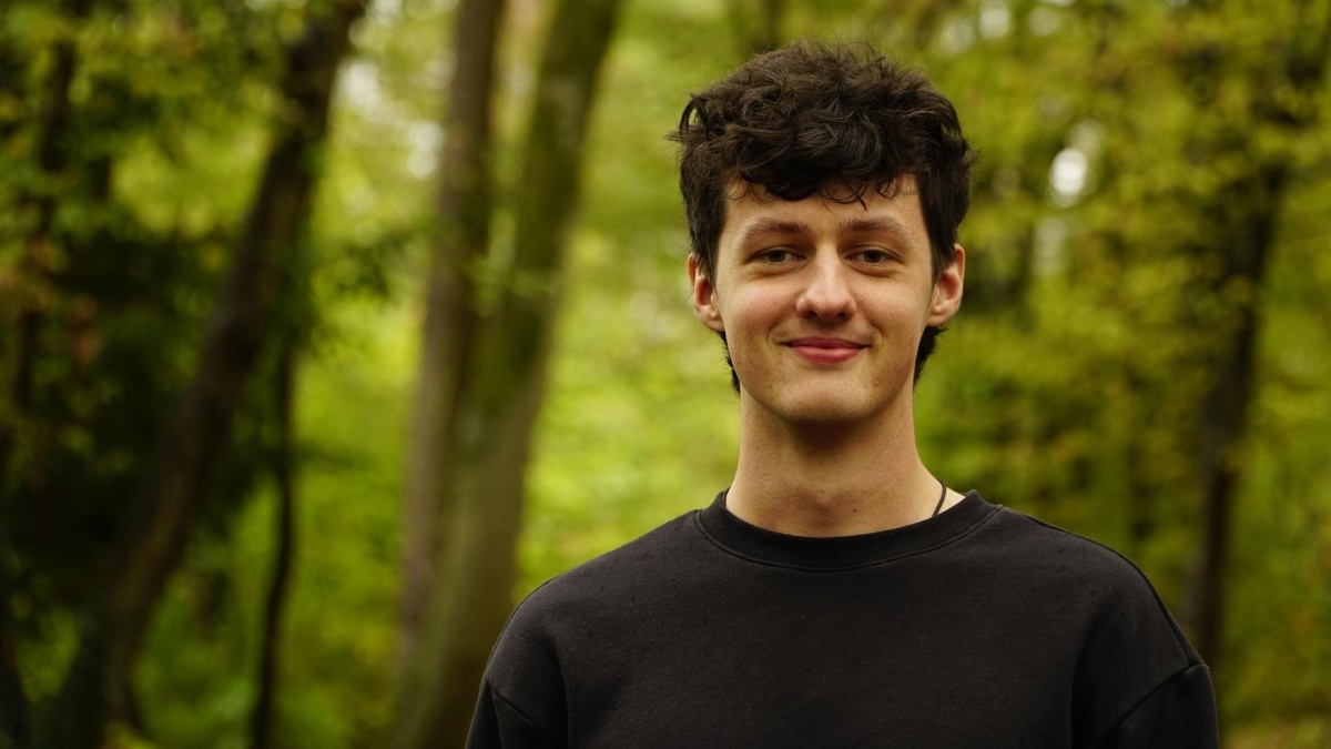 Max steht im Wald und lächelt in die Kamera.
