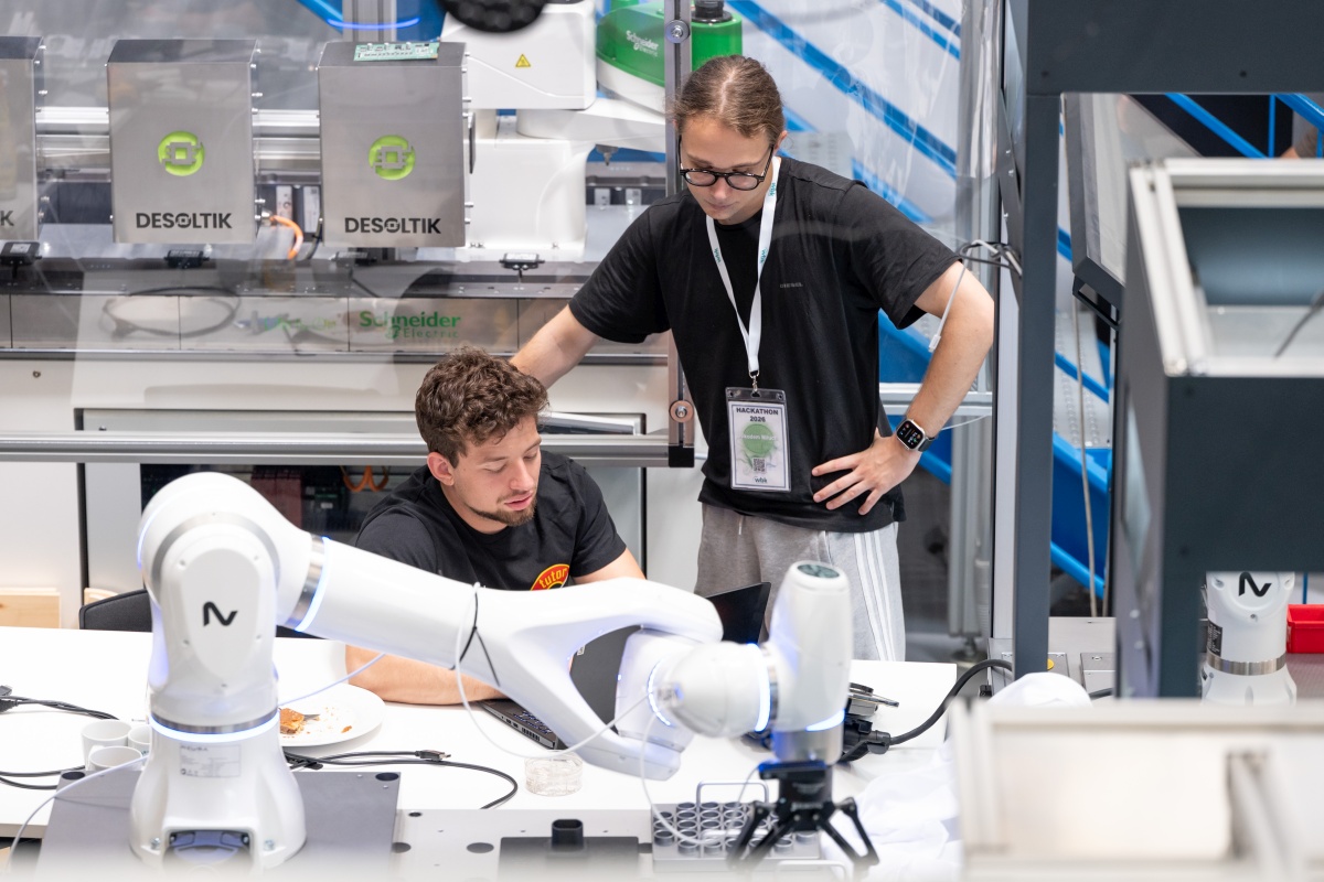 Zwei Personen arbeiten an einem Tisch mit Roboterarm.