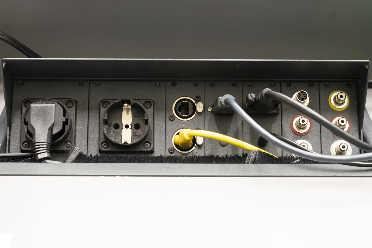 Strom- und Datenanschlüsse mit eingesteckten Kabeln in einem Schaltkasten.