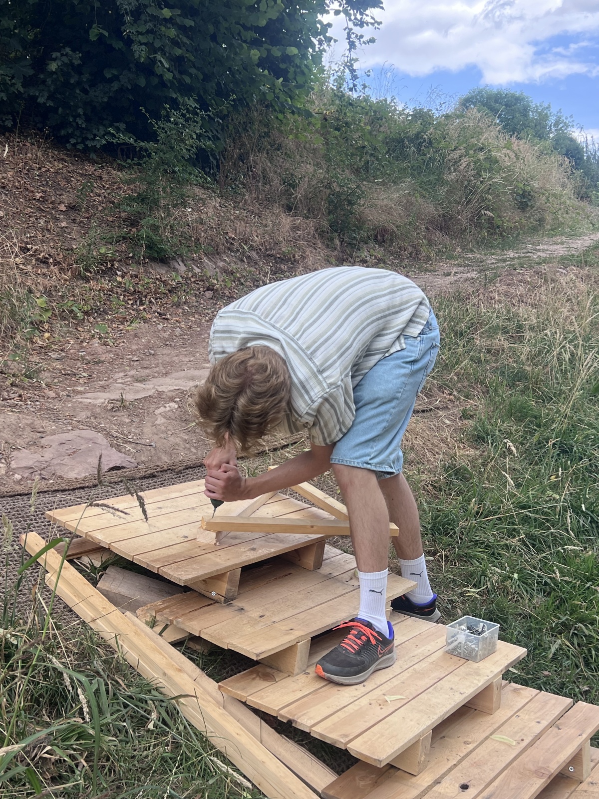 Junger Mann baut im Freien eine Konstruktion aus Holzpaletten.