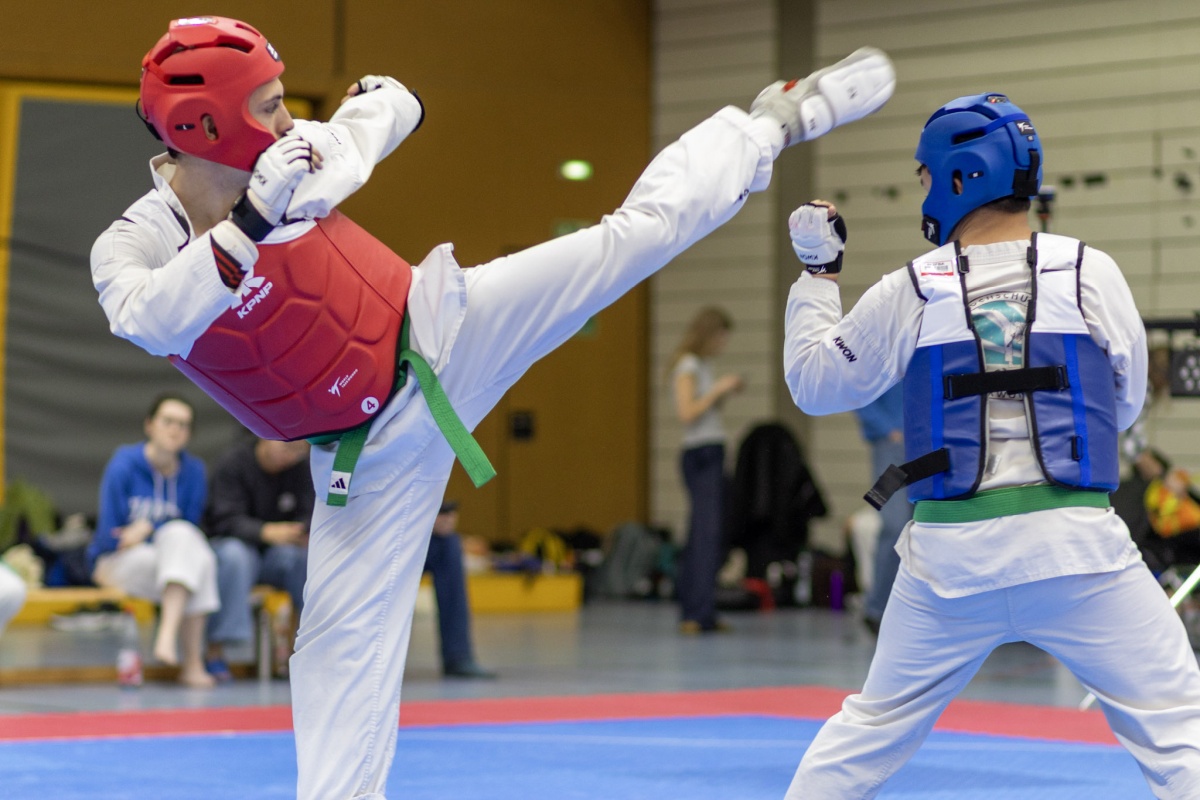 Kampfsportler in Schutzausrüstung führt hochkick gegen Gegner mit blaue Schutzausrüstung aus.